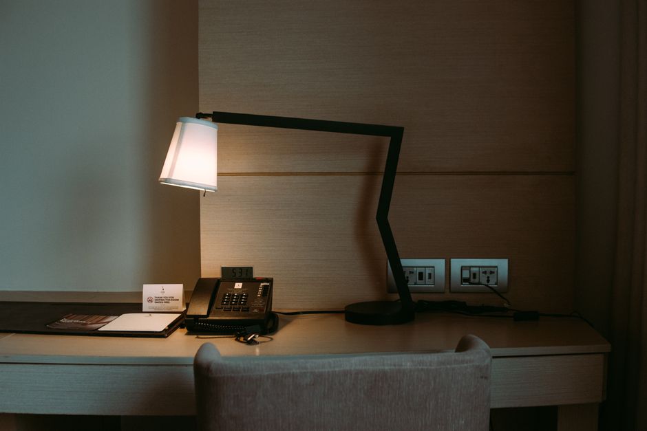 A modern hotel room desk featuring a stylish lamp, telephone, and stationery set.