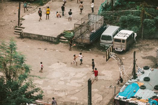 Aerial view of children playing basketball on a street court surrounded by vehicles and urban structures.