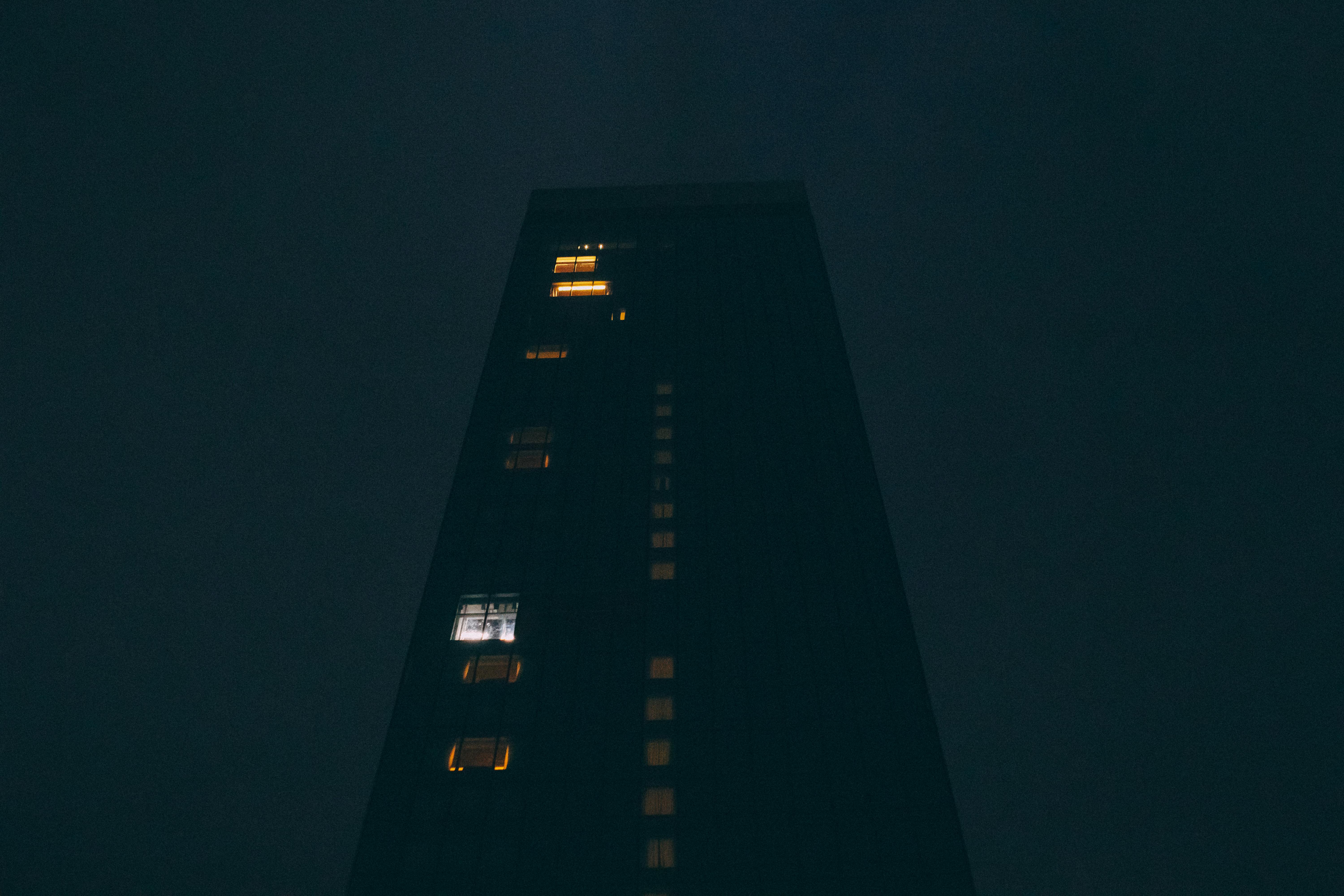 Moody nighttime view of a tall skyscraper with illuminated windows against dark sky.