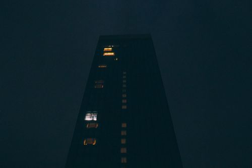 Free Moody nighttime view of a tall skyscraper with illuminated windows against dark sky. Stock Photo