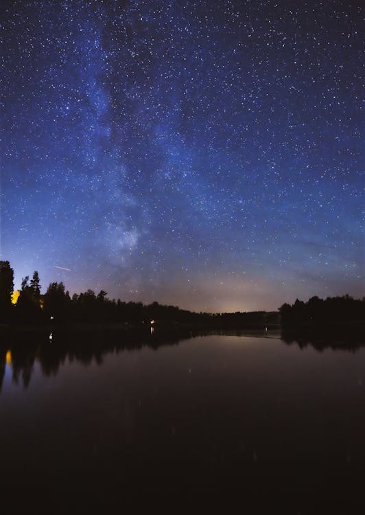 Landscape Photography of Tree's Reflection on Body of Water Under a Starry Night Sky