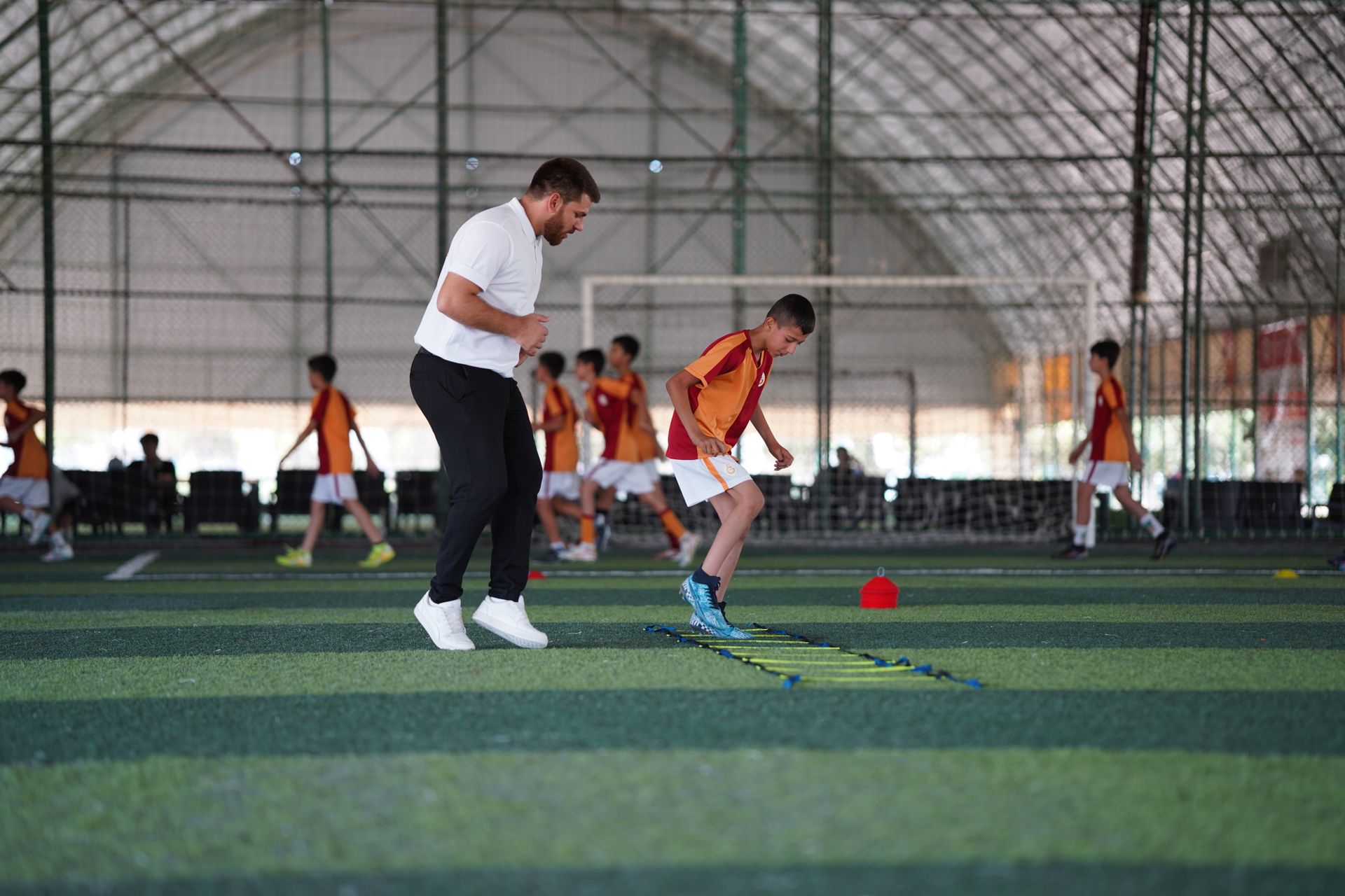 A coach running an agility drill with a young boy on an indoor turf field