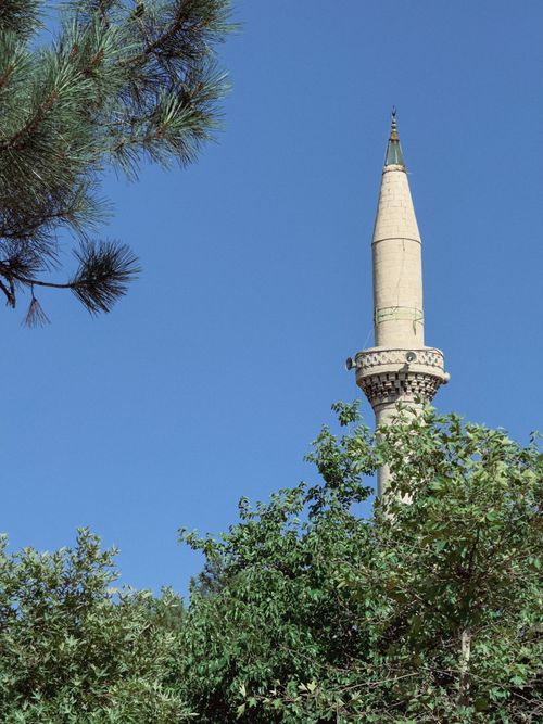 Free A picturesque minaret rises above green trees under a vibrant blue sky in Elâzığ, Türkiye. Stock Photo