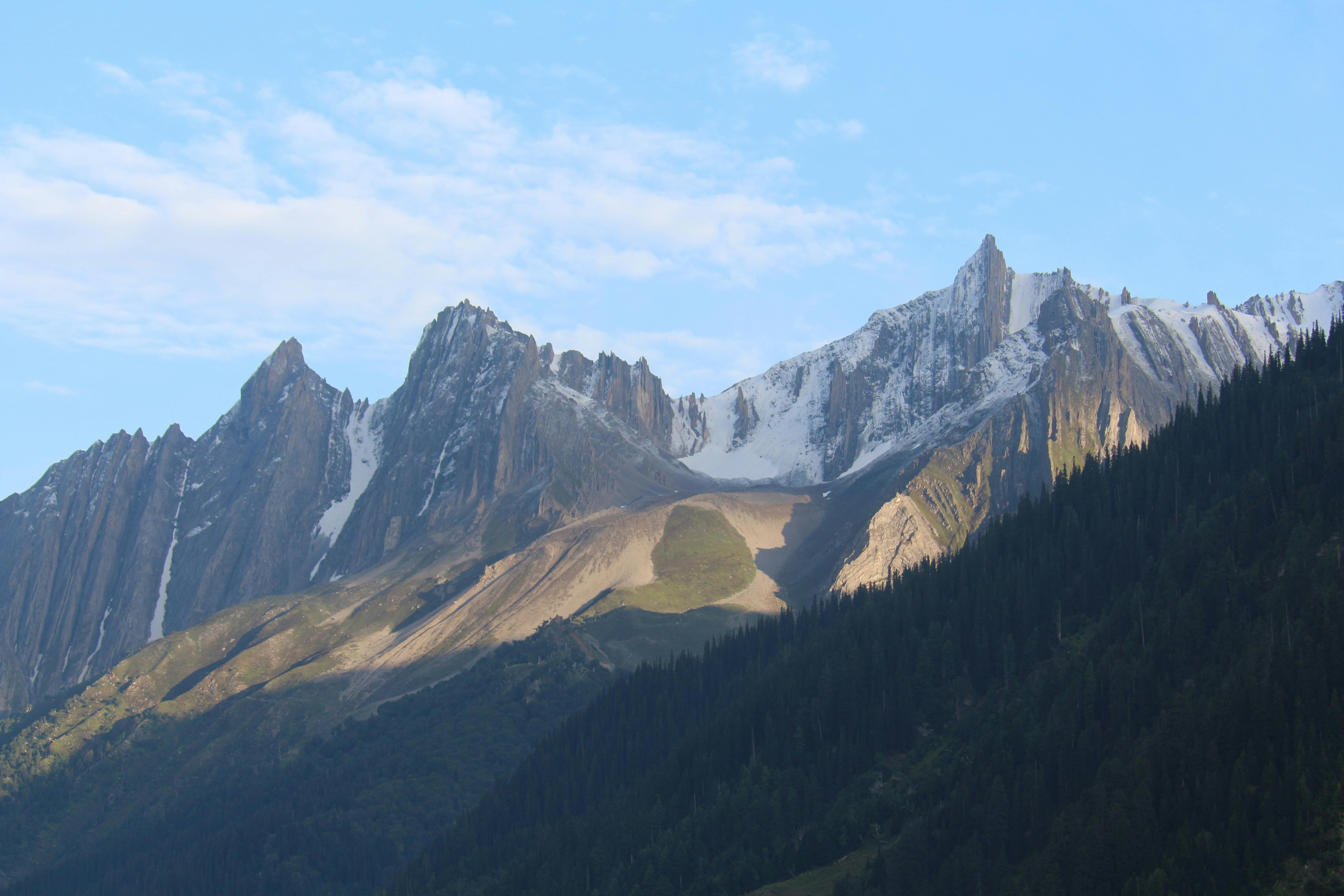 A breathtaking view of a majestic mountain range with snowy peaks under a clear blue sky at sunrise.