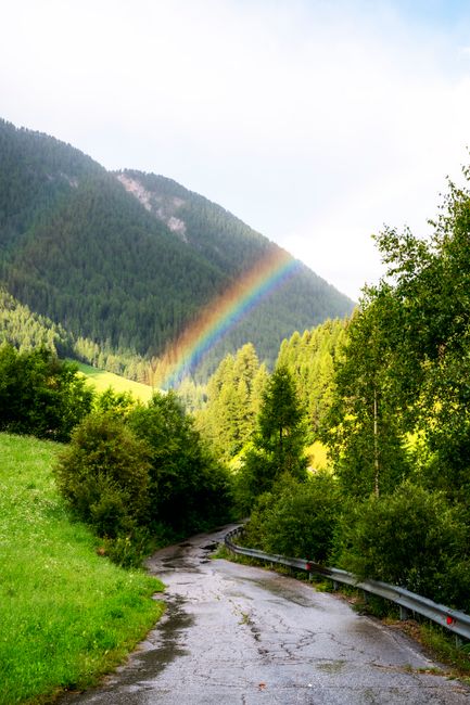 Scenic view of a rainbow arching over a lush mountain landscape with a winding pathway, captured in spring.