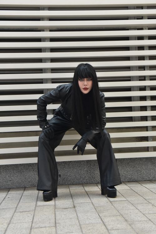 Free Stylish woman wearing black leather outfit posing against striped background outdoors. Stock Photo