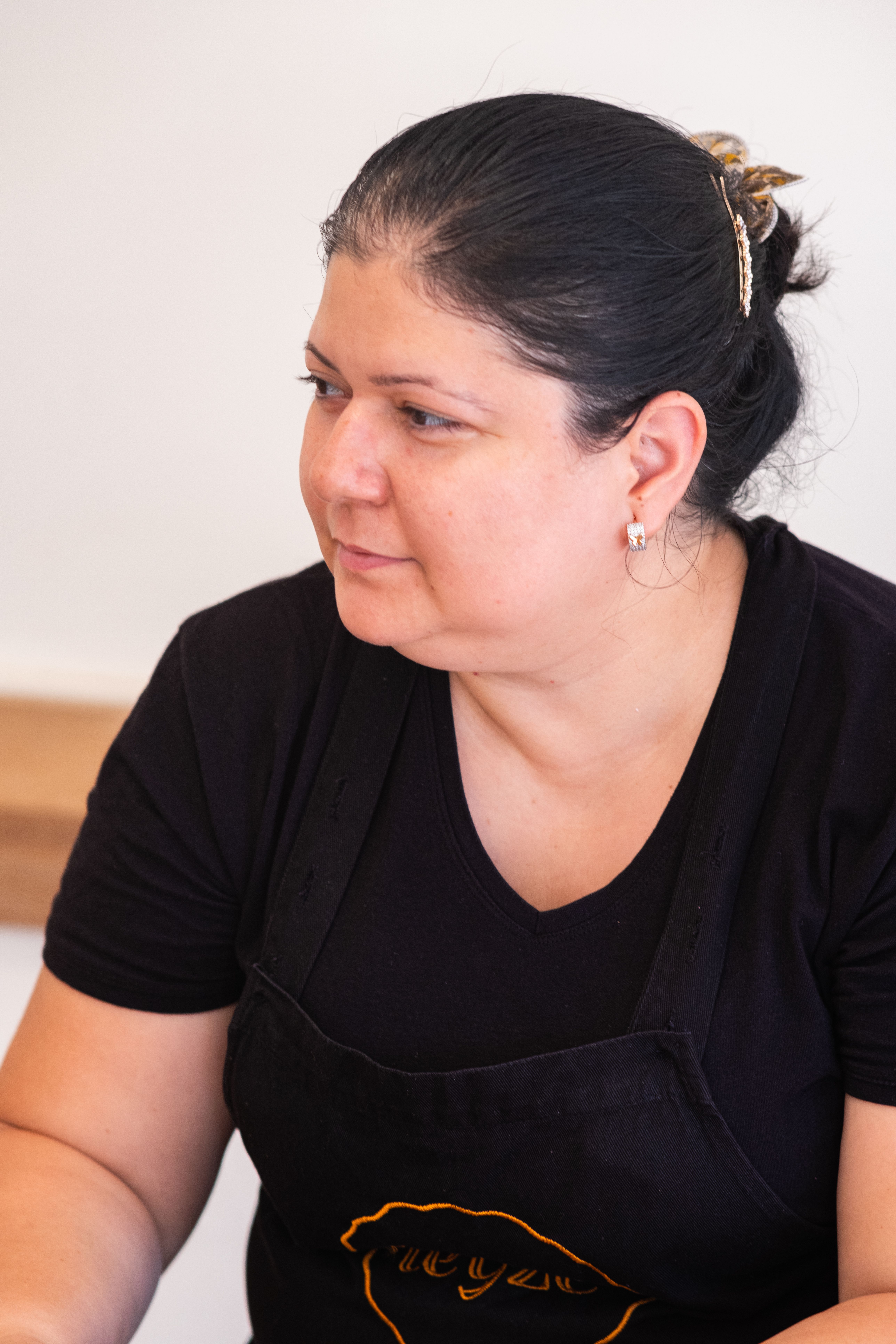 Close-up portrait of a woman wearing a black apron, taken indoors with soft lighting.