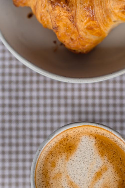 Free Top view of a croissant and coffee cup on a checkered tablecloth, perfect for breakfast themes. Stock Photo