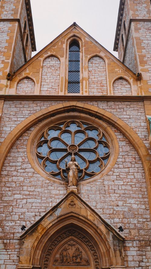 Free The intricate facade of a Gothic church featuring an ornate rose window and statues. Stock Photo