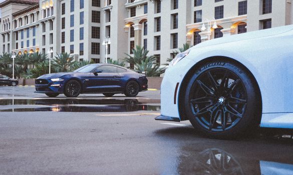 Luxury cars parked in front of a stylish building with reflective wet pavement.