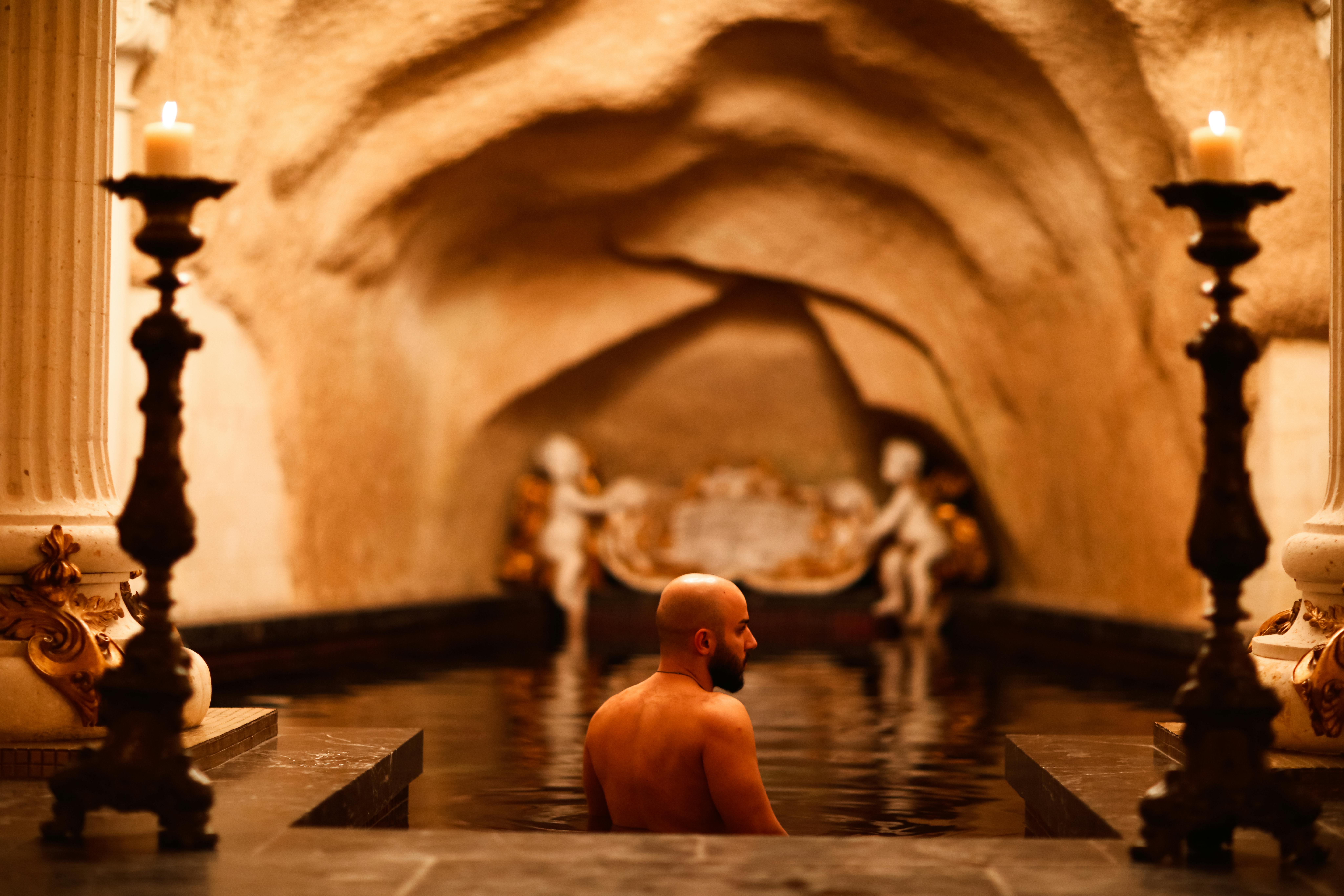 Une scène sereine d'un homme se détendant dans un bain intérieur opulent éclairé aux bougies avec des sculptures classiques.