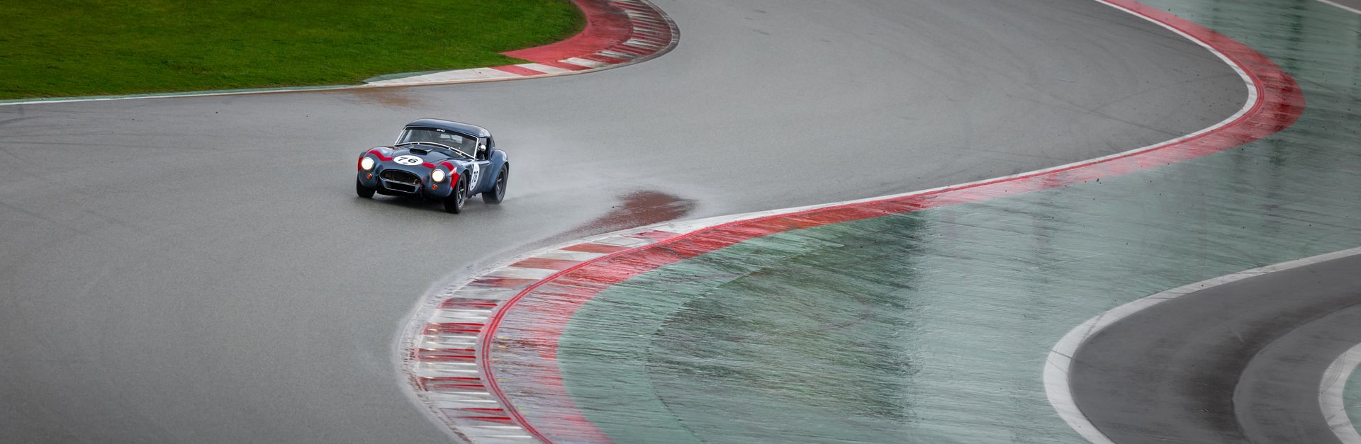 Vintage sports car navigating a wet racetrack curve with speed and agility.