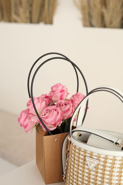 Free Chic arrangement of pink roses in a paper bag beside a designer handbag. Stock Photo