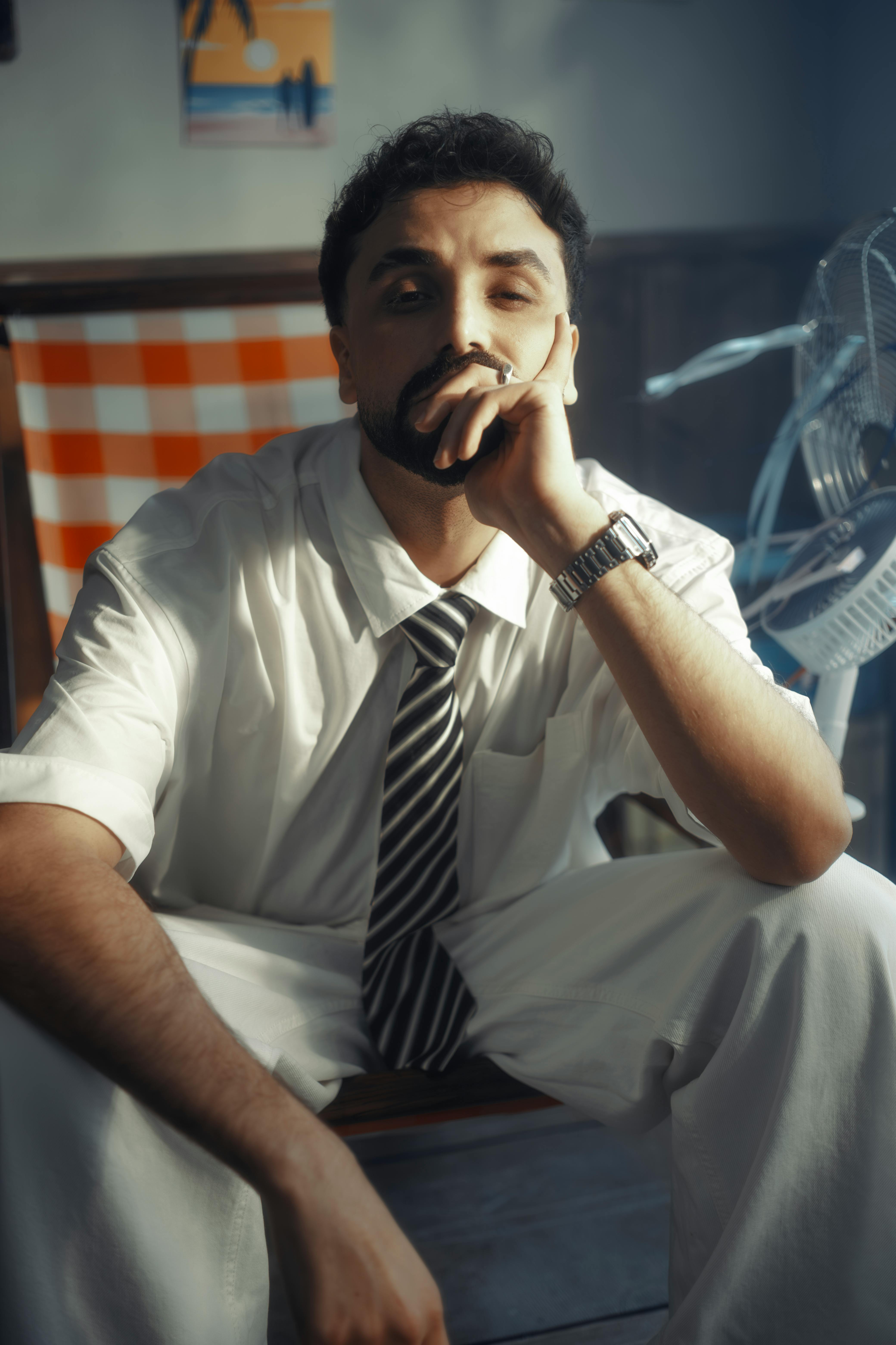 Ilmainen Sisällä istuu mietteliäs mies valkoisessa paidassa ja solmiossa, kuva pehmeässä valossa. Kuvapankkikuva