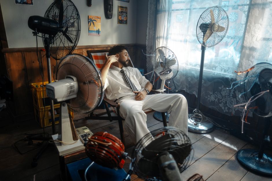 Man in white suit relaxing amongst multiple fans in a retro-themed room.
