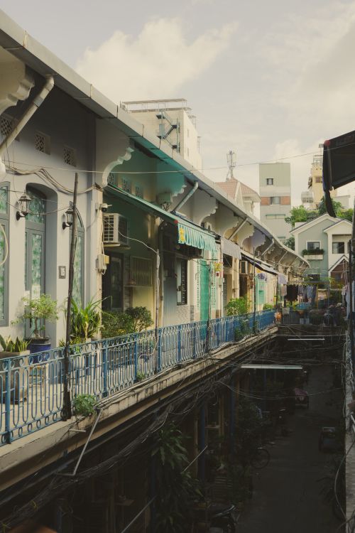 Free A vintage-style Vietnamese balcony scene featuring colorful buildings, lush plants, and a bright sky. Stock Photo