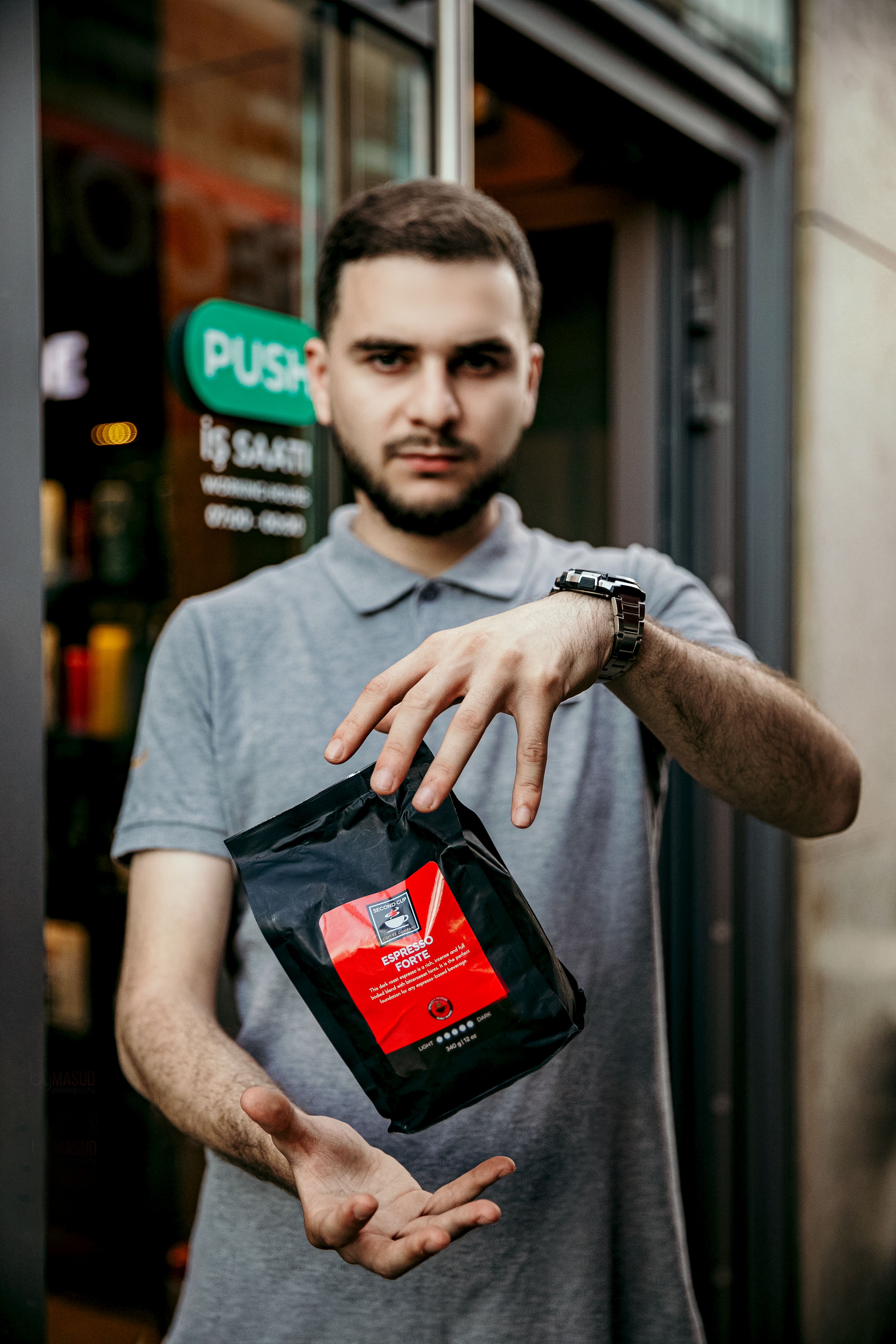 Young barista showcasing a bag of premium coffee outside a Baku coffeeshop.