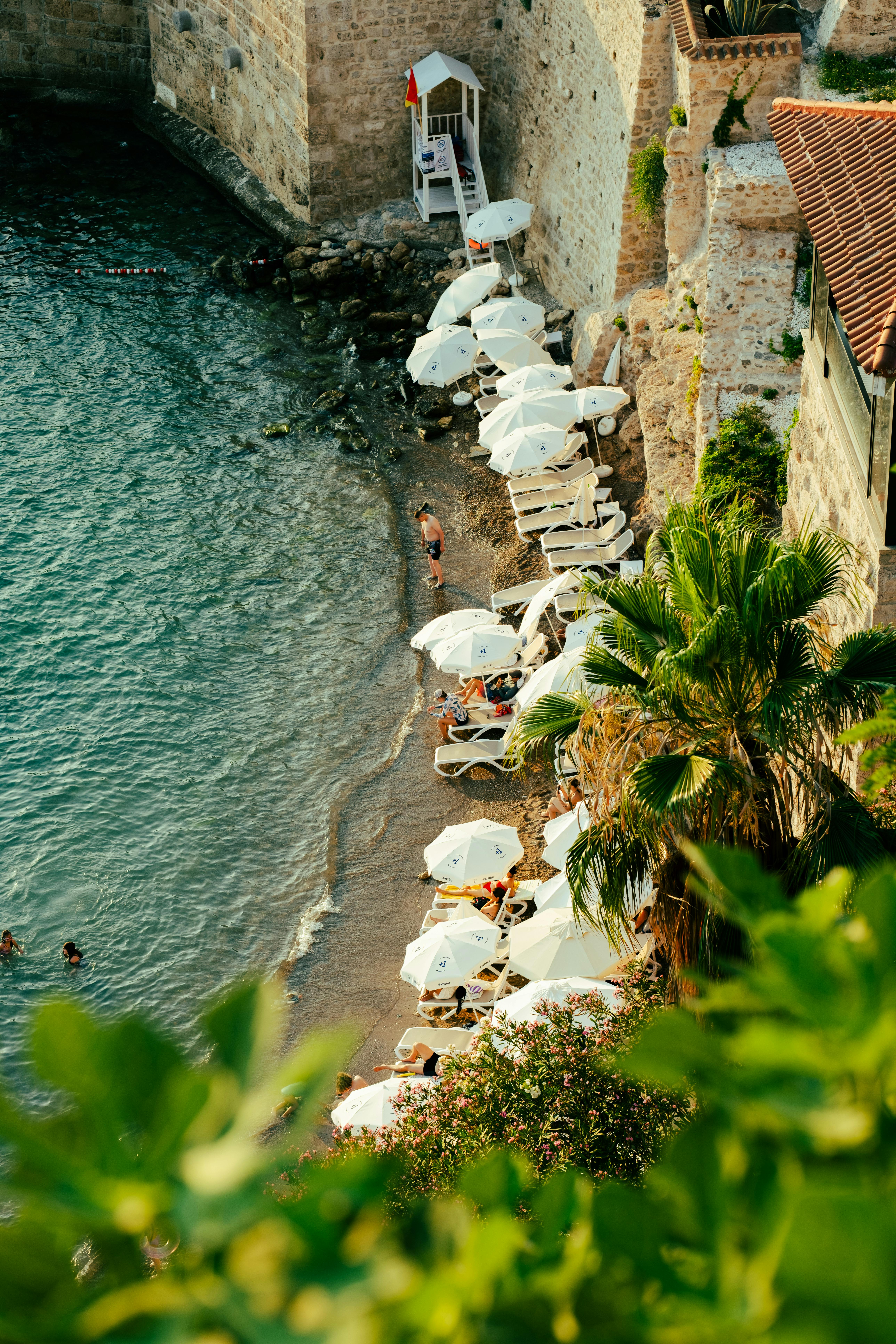 Serene beachfront with parasols and palm trees by a historic stone wall.