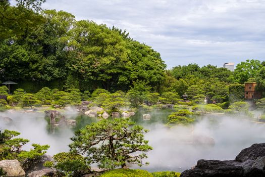Tranquil Japanese garden featuring lush greenery, a misty pond, and decorative rocks.