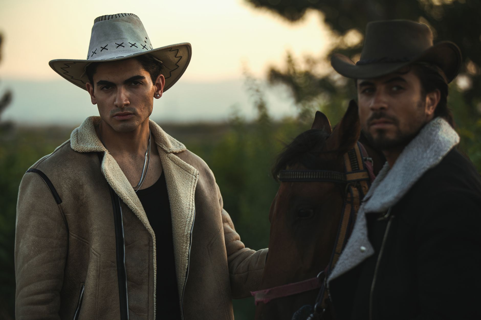 Two cowboys with a horse during sunset in a Western style scene.