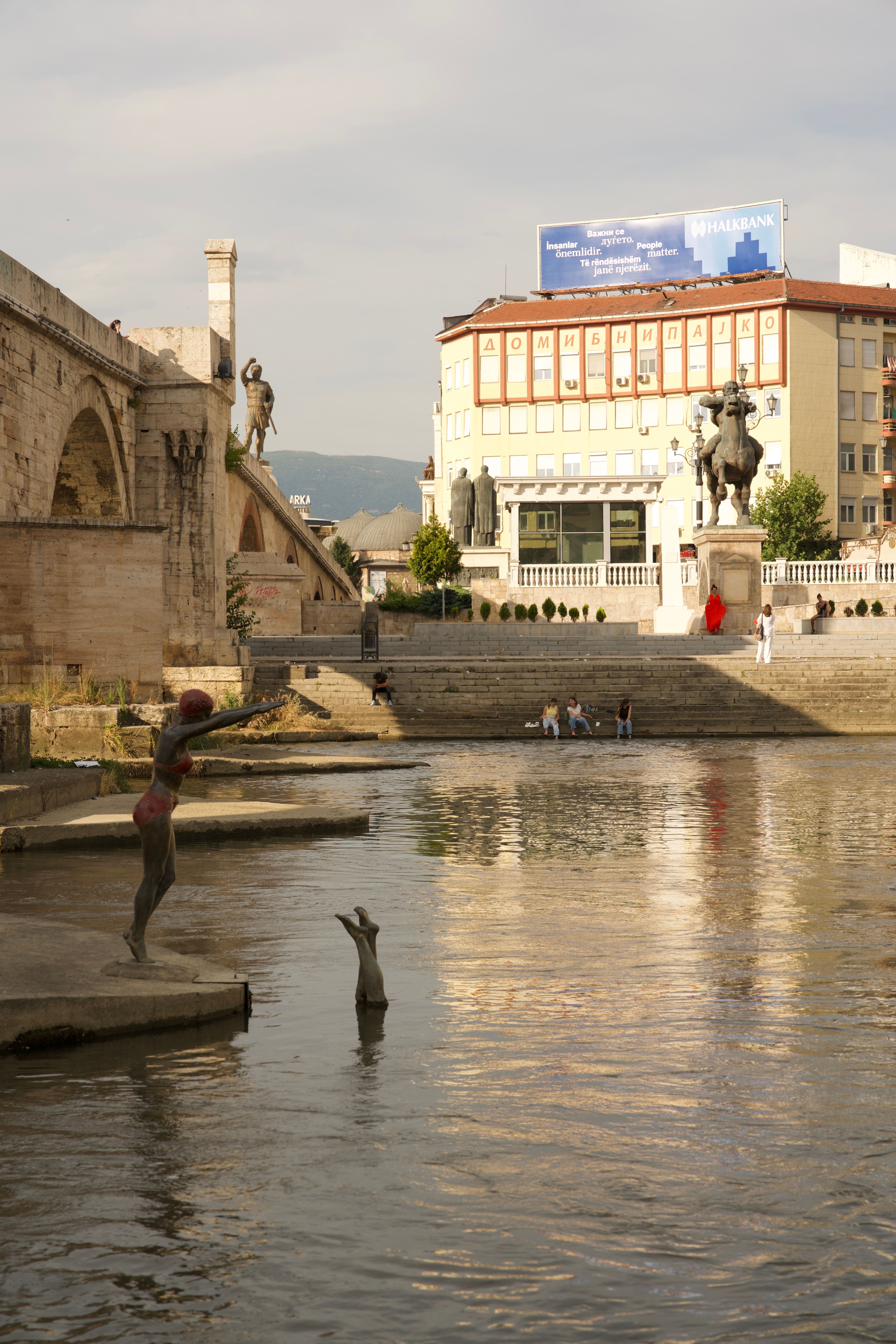 View of Skopje riverfront featuring iconic statues against a cityscape.
