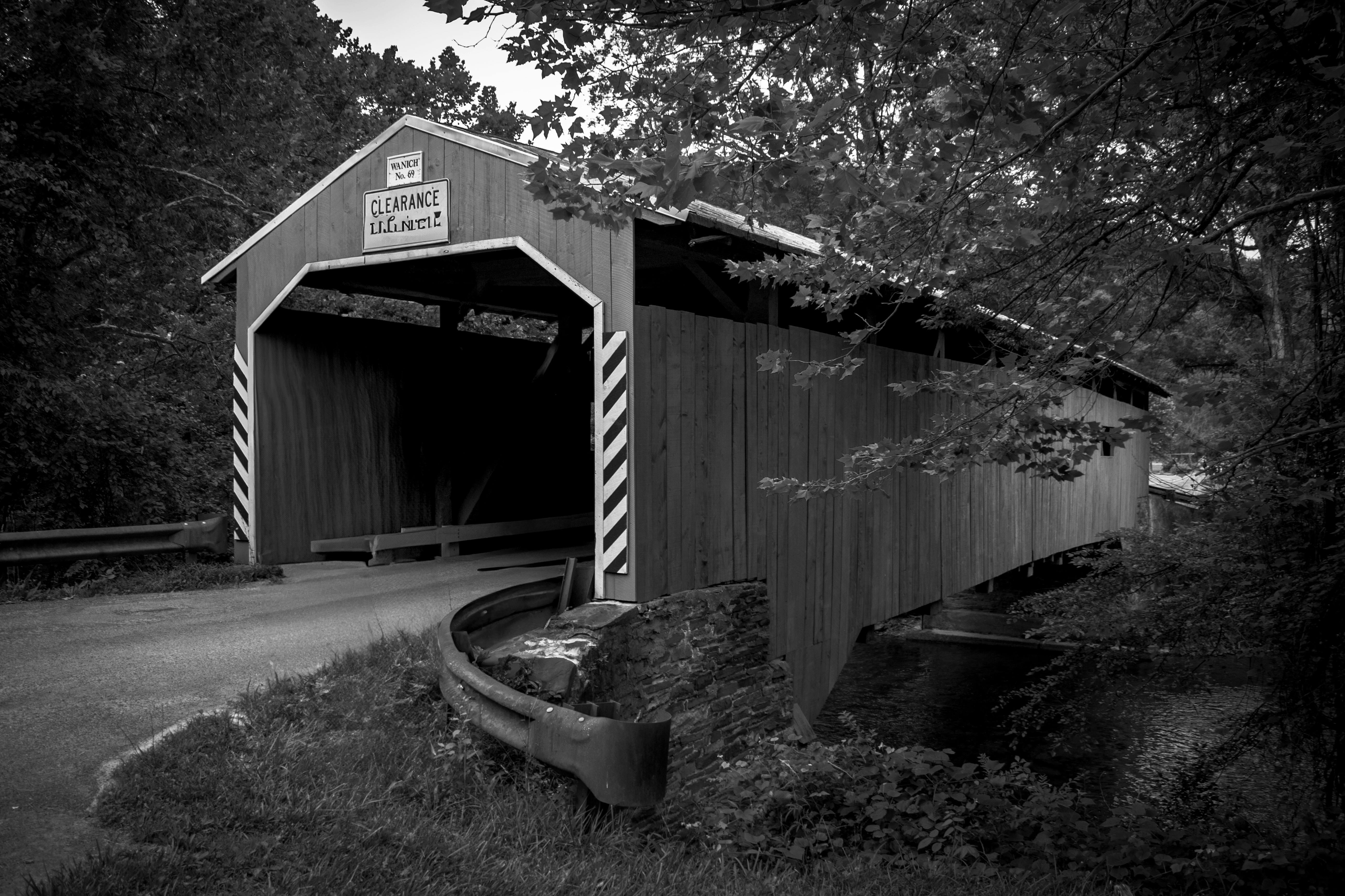 Historic covered bridge in a serene forest setting captured in monochrome.
