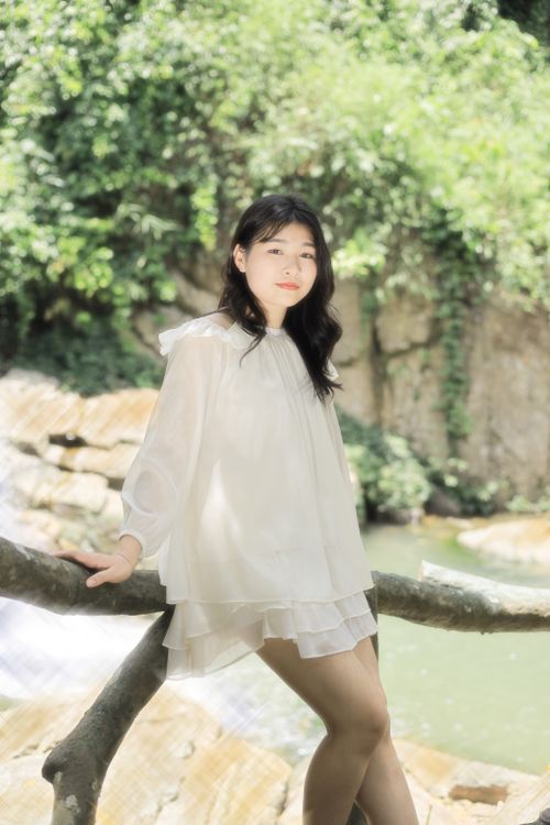 Free A young woman enjoys a serene moment by a lush waterfall in sunlight. Stock Photo
