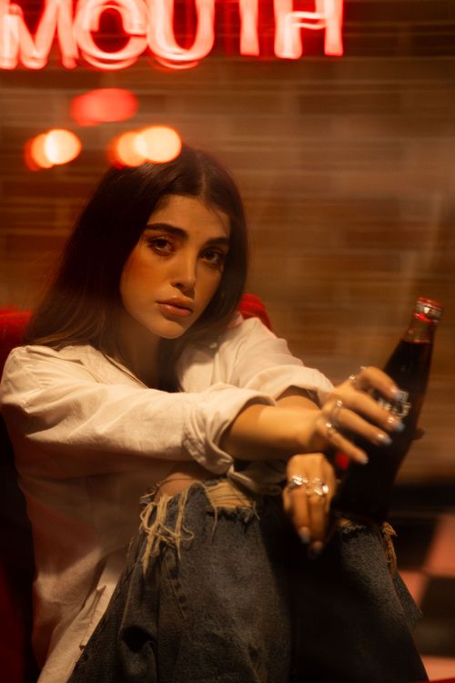 Free Stylish woman in cozy café setting holding a drink. Warm tones and casual fashion. Stock Photo