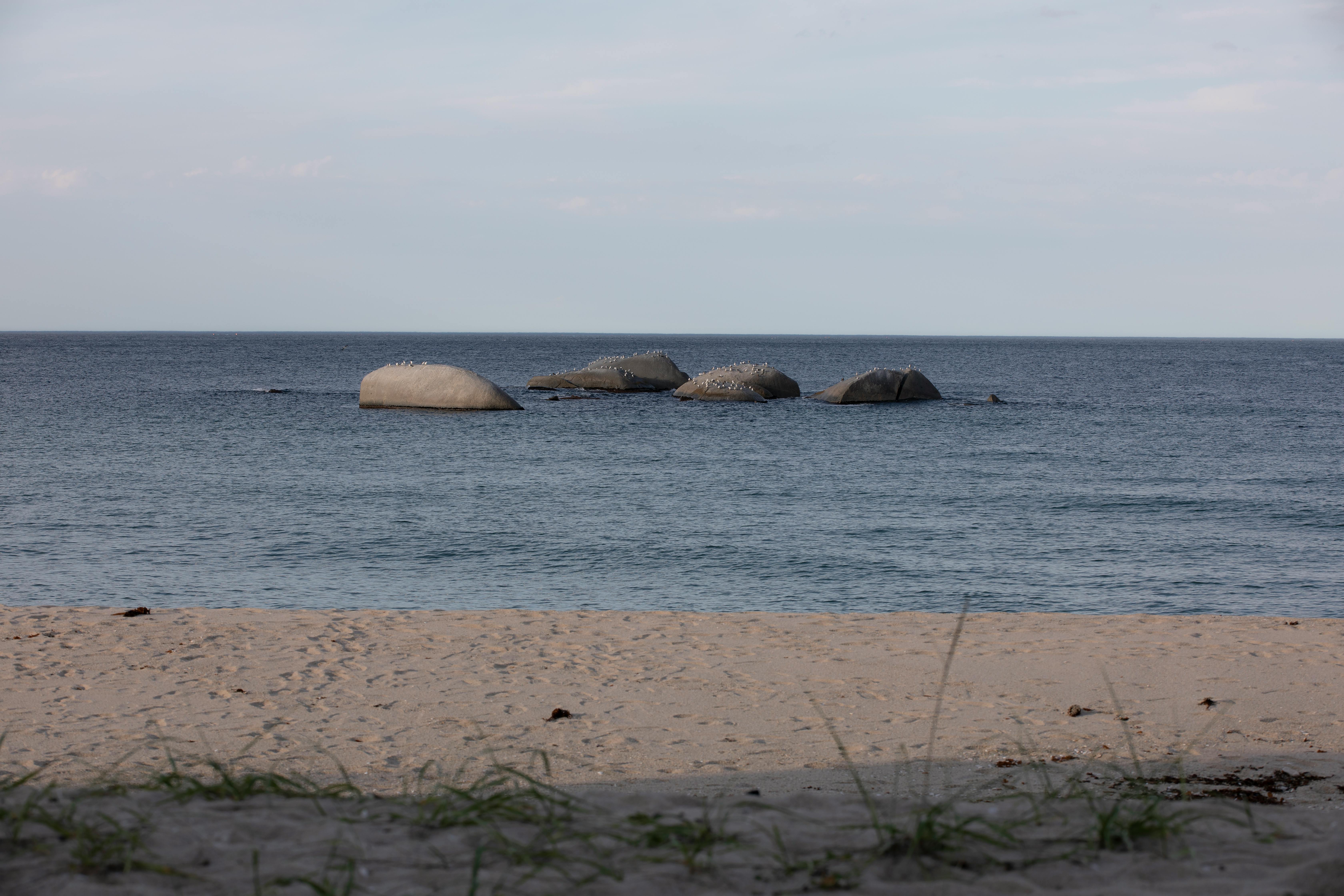 Peaceful beach scene with calm ocean waves and rock formations under a clear sky.