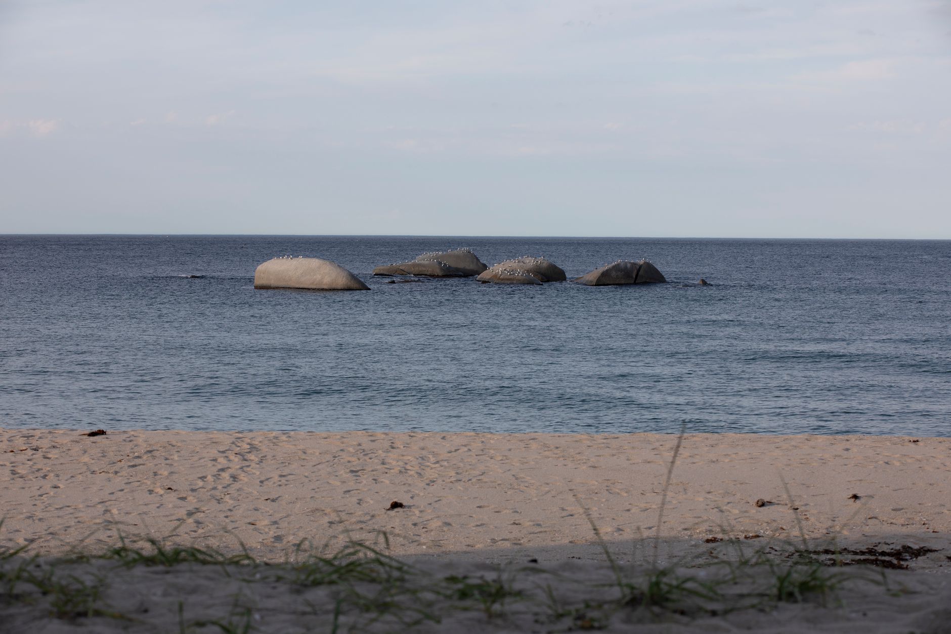 Peaceful beach scene with calm ocean waves and rock formations under a clear sky.