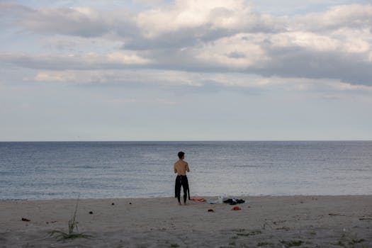 A lone person stands by the ocean under a cloudy sky, capturing solitude and serenity.