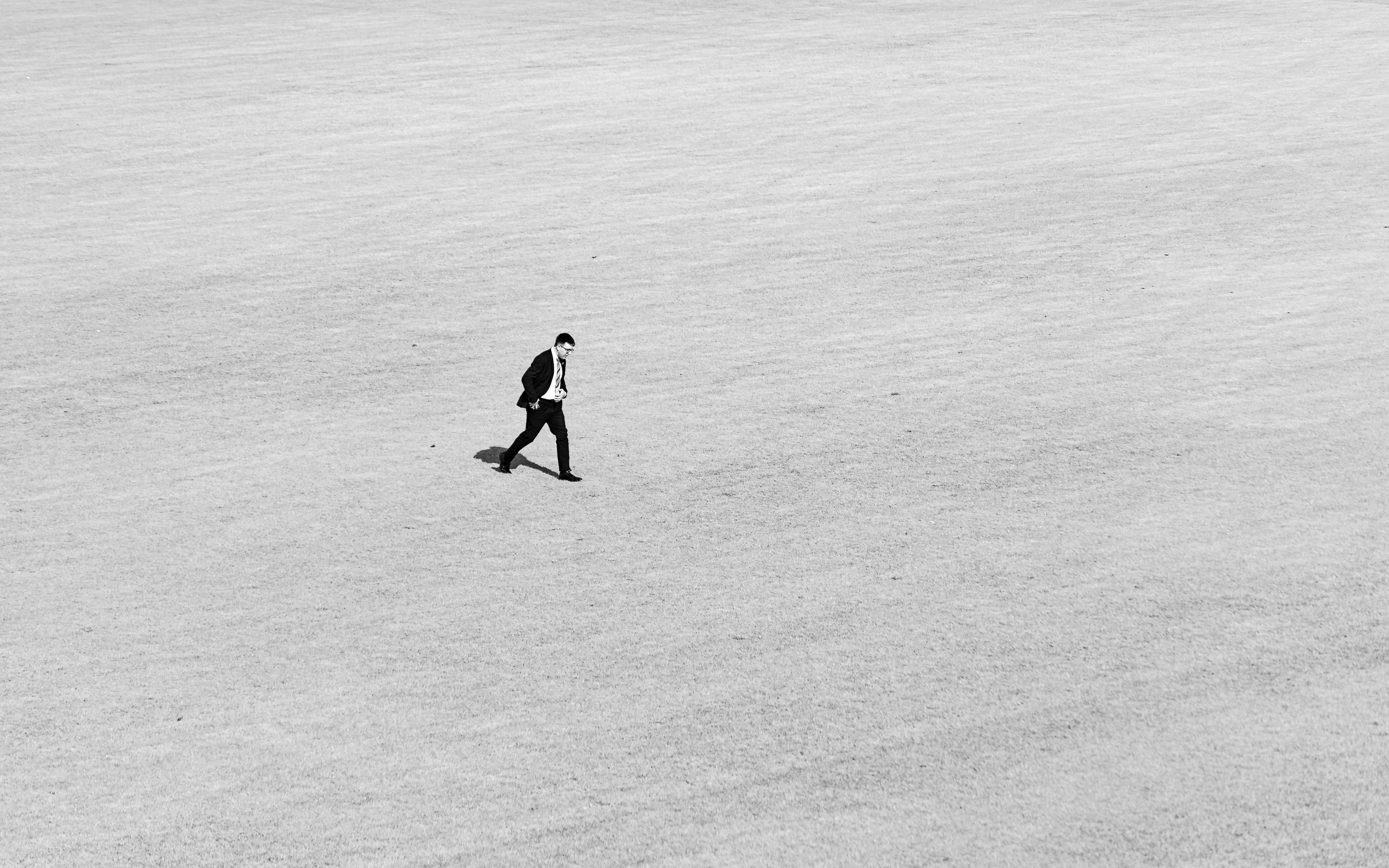 A solitary businessman walking across an expansive field in black and white.