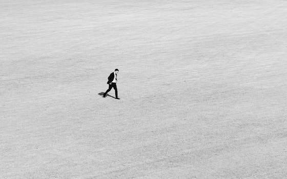 A solitary businessman walking across an expansive field in black and white.