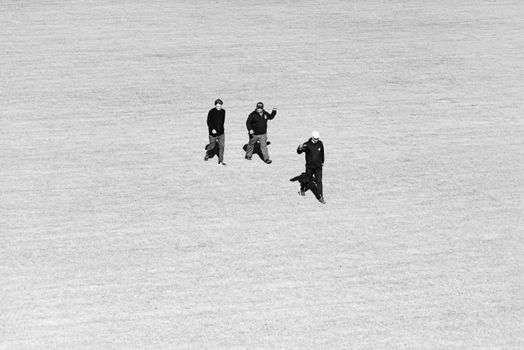 Aerial view of three individuals walking across a vast field, captured in black and white.