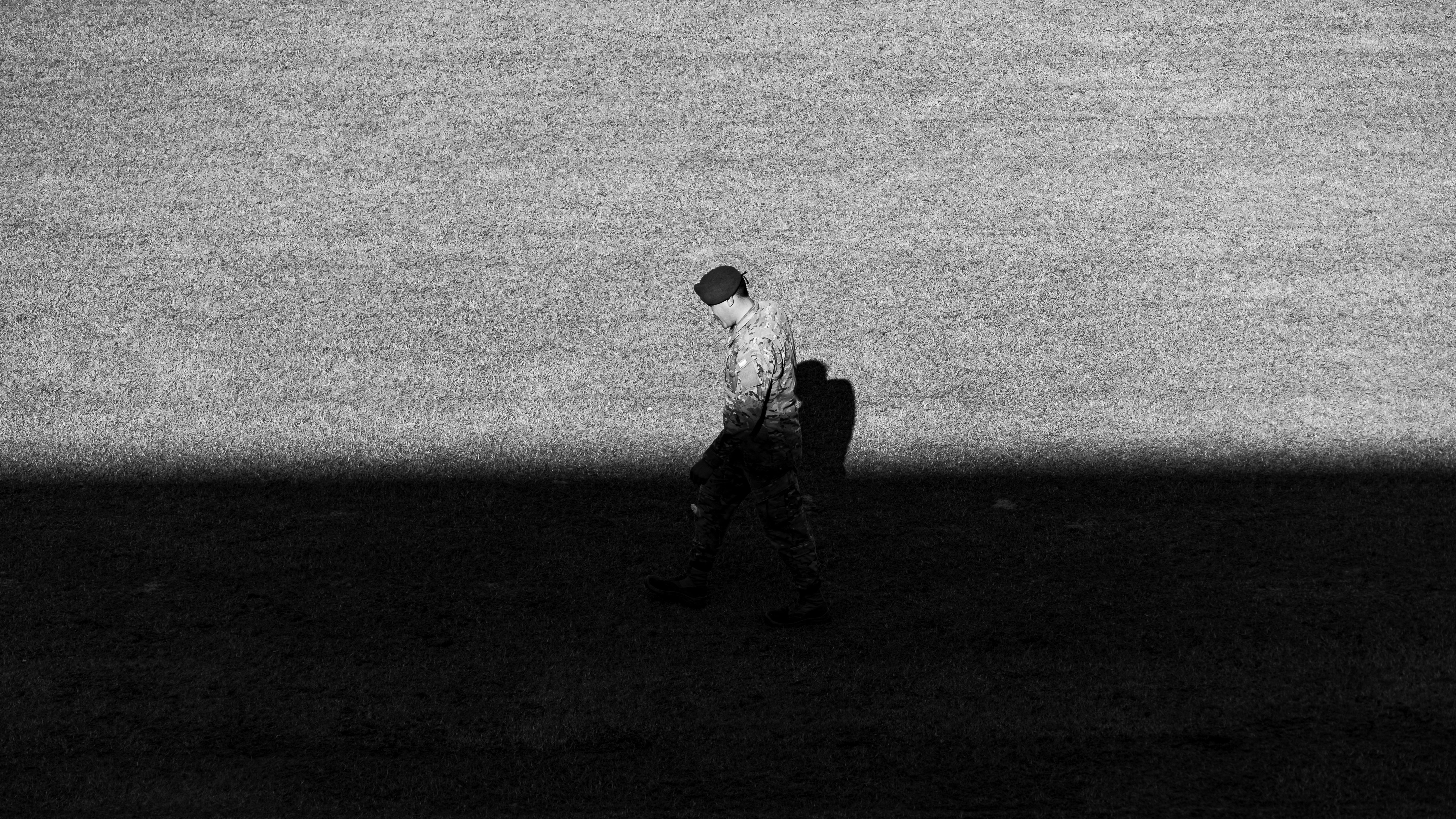 Black and white image of a soldier walking in a shadowed area.