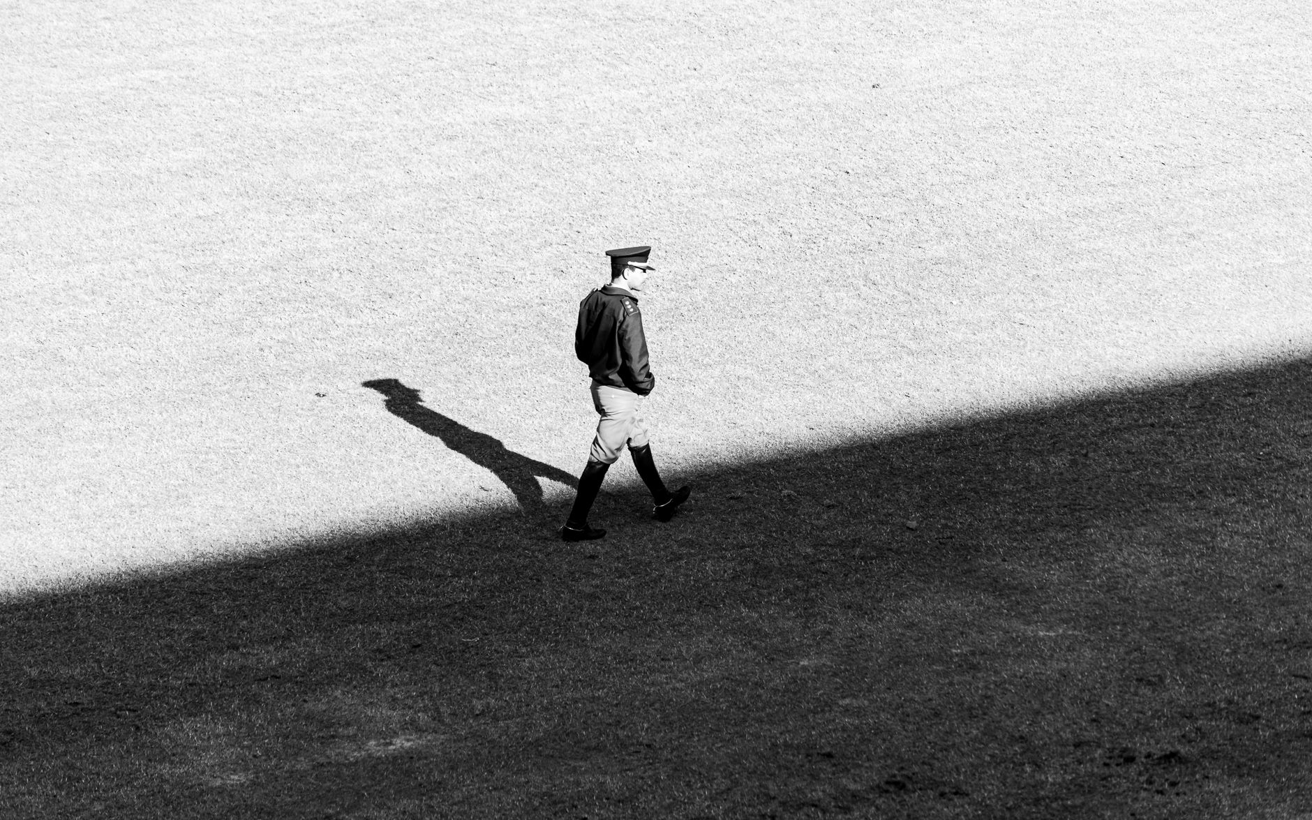 A lone guard in uniform walks across a shadowed field in a striking black and white photograph.