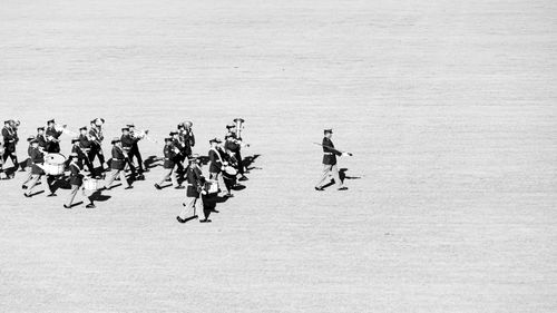 Free Black and white photo of a marching band in uniform practicing on an open field. Stock Photo