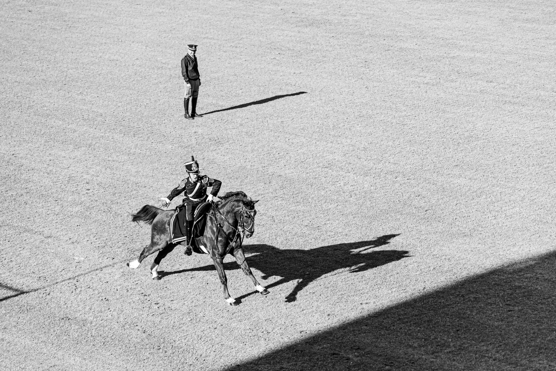 A military rider performs dressage on a field while an officer observes, captured in black and white.