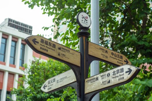 Directional street signs in a Chinese city with lush greenery and buildings in the background.