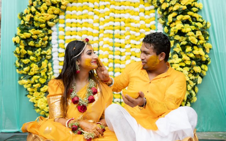 A couple at their haldi ceremony under a marigold arch