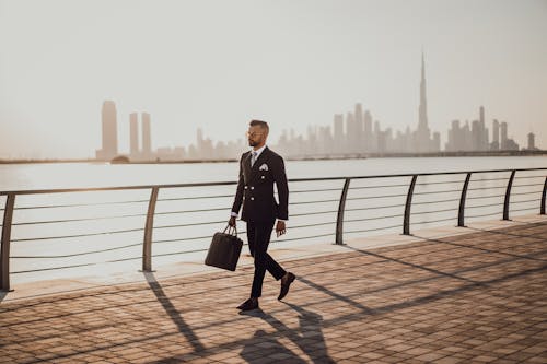 Man Walking on Pavement While Holding a Bag