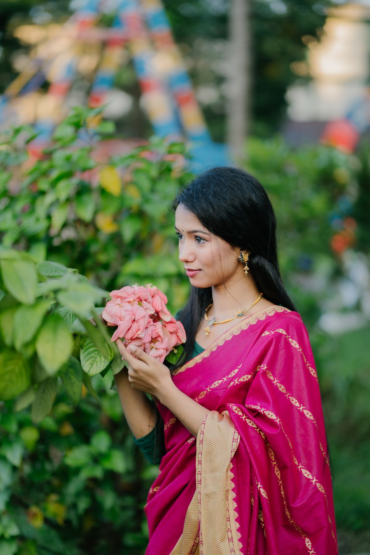 Woman in a magenta-pink saree holding flowers in a garden