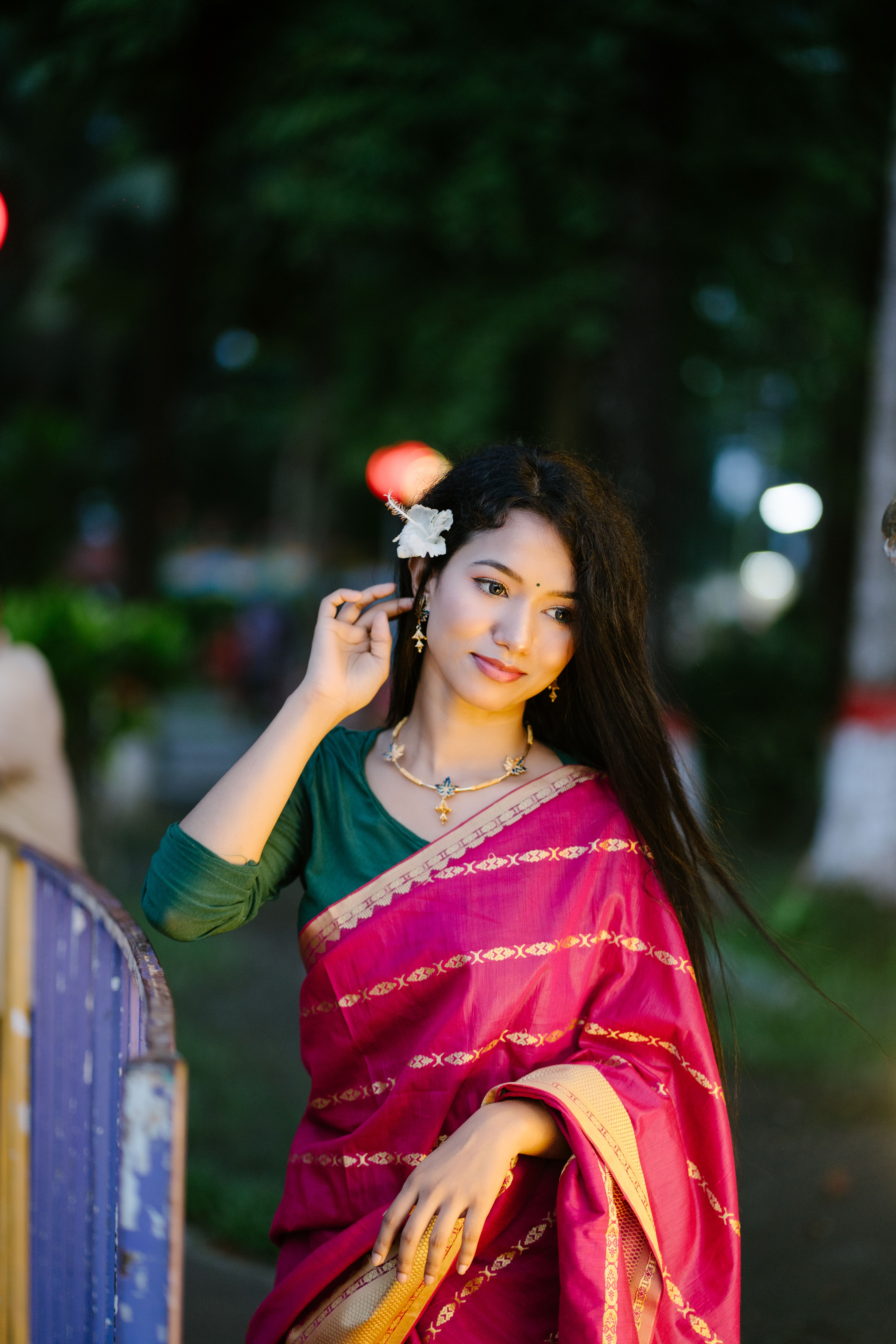 Portrait of a woman wearing a pink sari and floral hair accessory, standing outdoors.