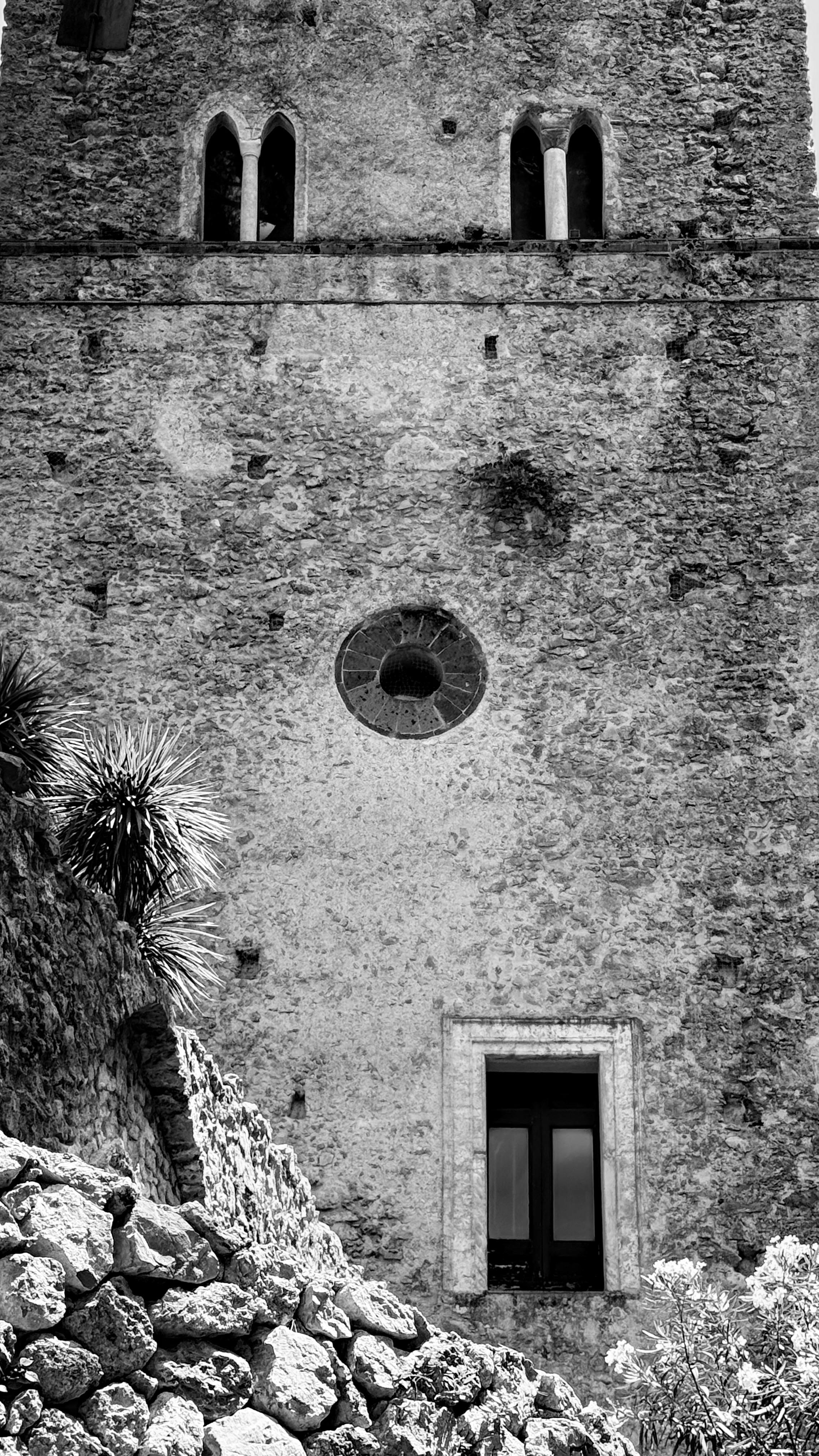 Black and white photo of an ancient stone wall featuring arches and circular window.