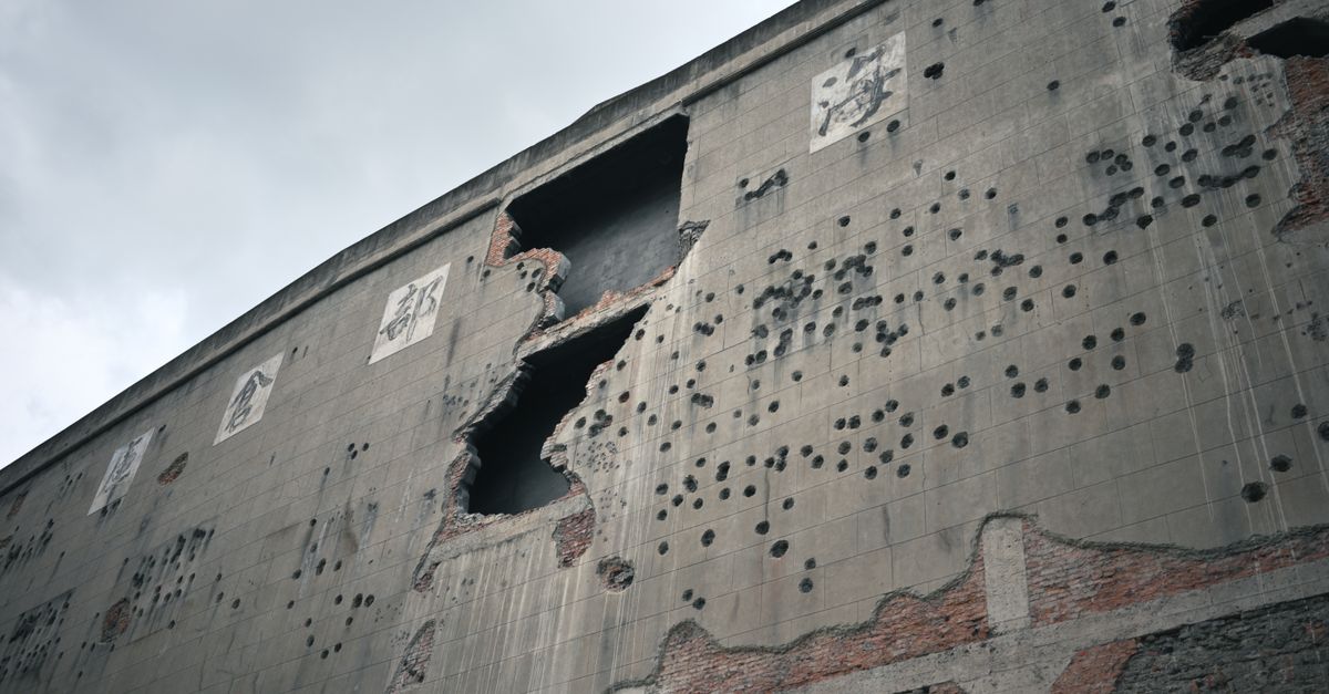 A damaged building facade showing signs of war and decay under a cloudy sky.