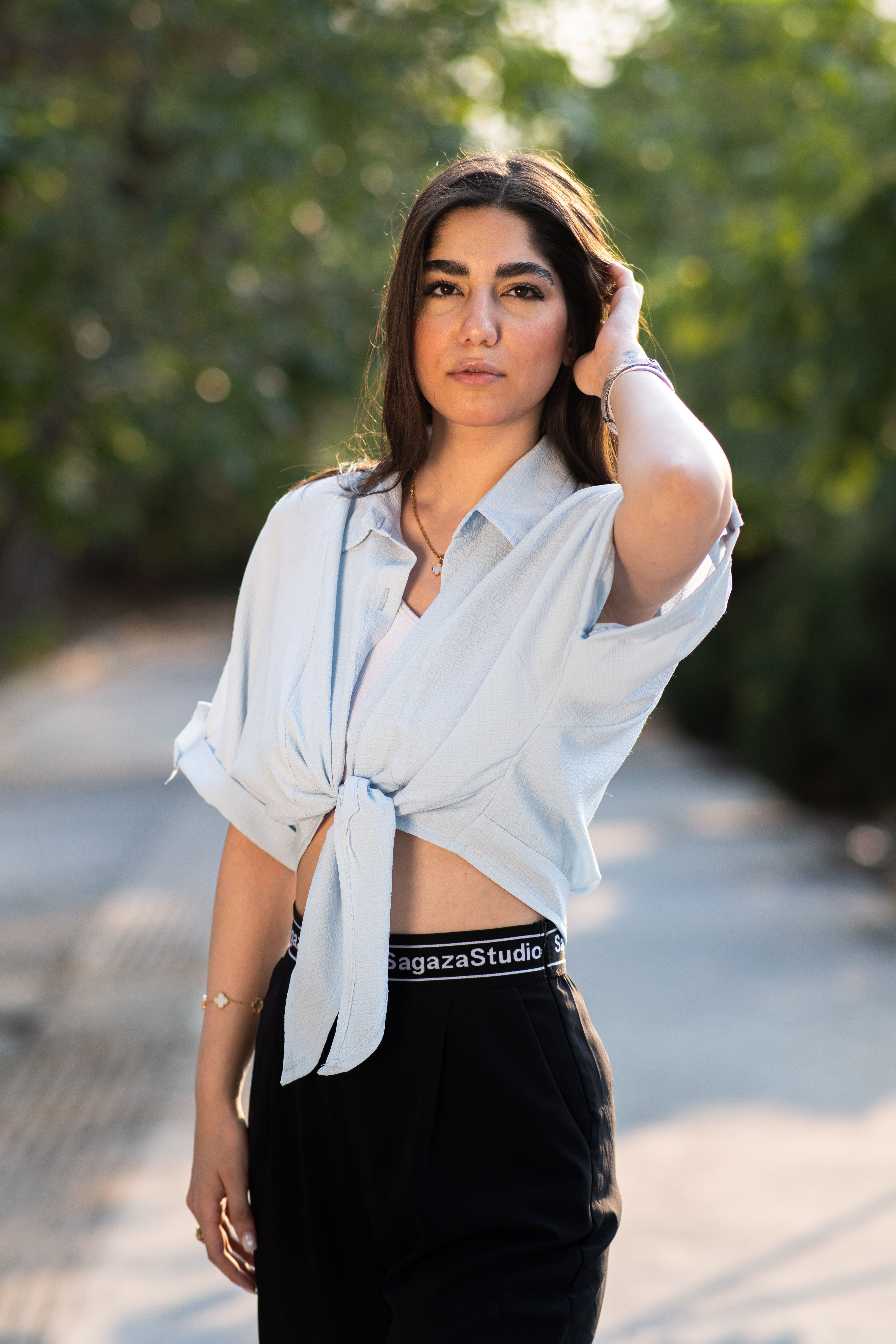 Stylish portrait of a woman standing outdoors in summer light, showcasing fashion and elegance.