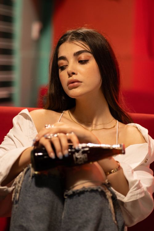 Free Stylish woman in casual attire holding a soda bottle indoors. Stock Photo
