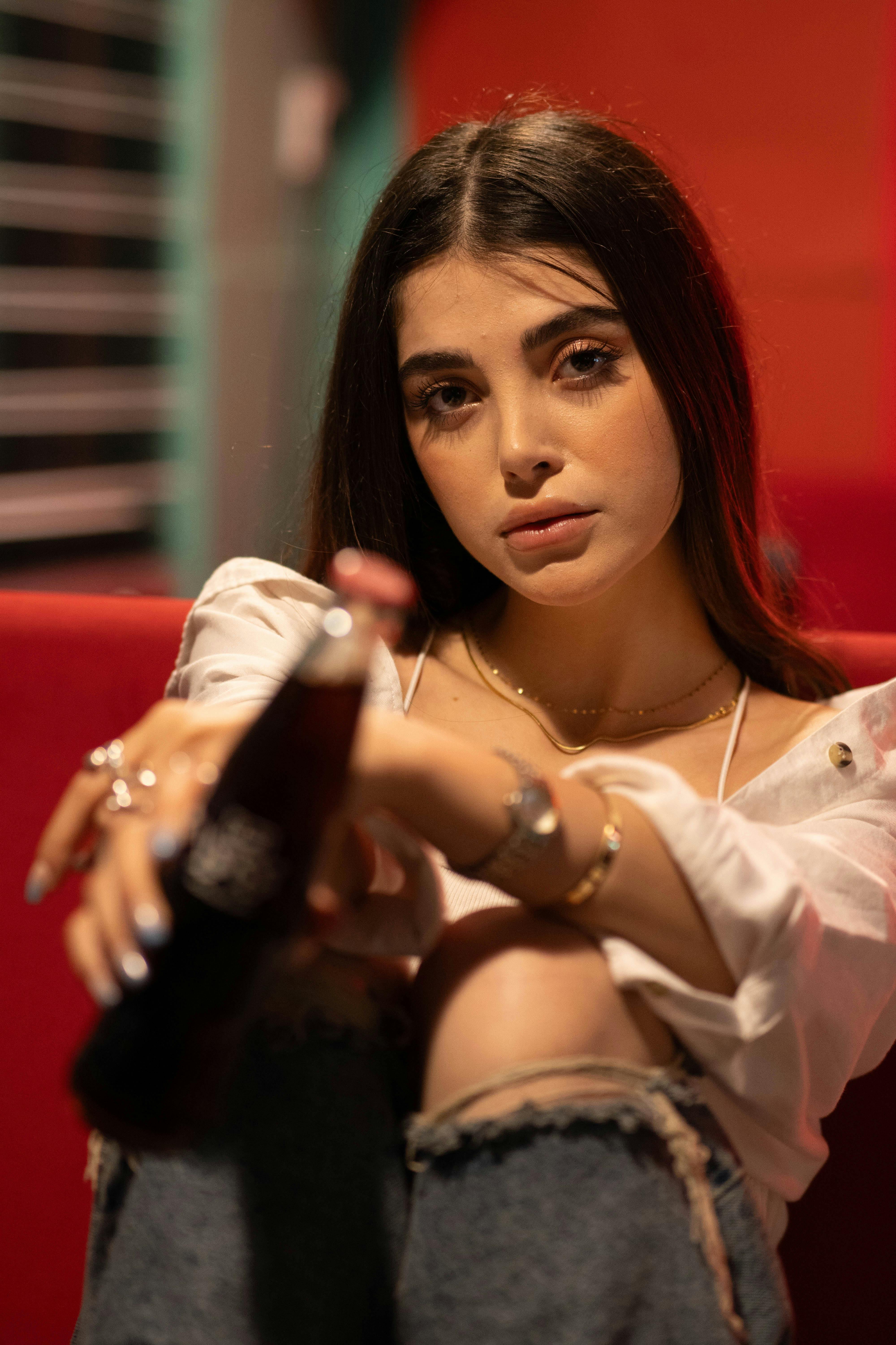 A captivating portrait of a young woman holding a soda bottle in a vibrant setting.