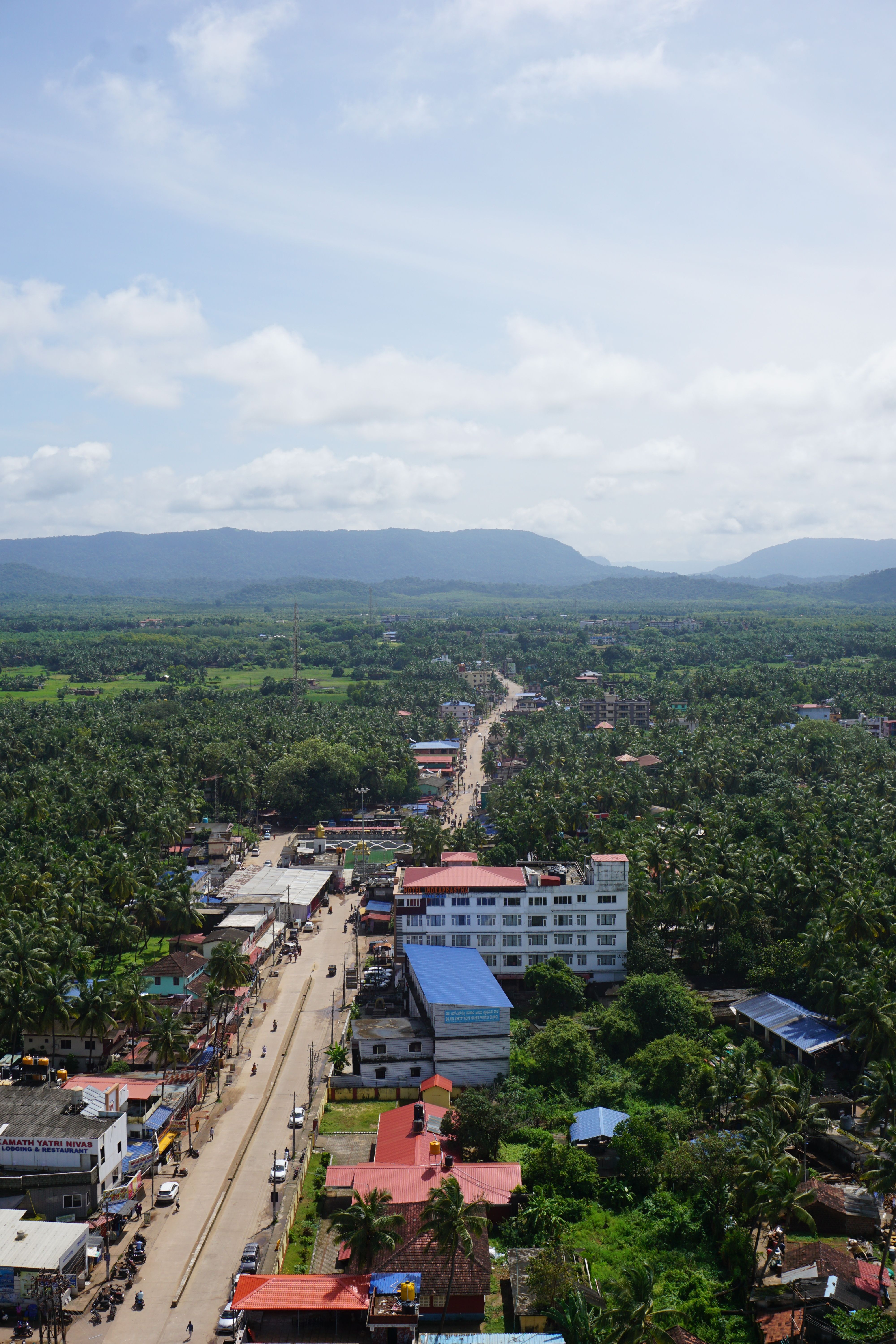Scenic aerial shot showcasing a lush green landscape, winding road, and distant hills under a bright sky.