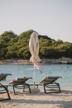 Relaxing beach chairs and umbrella by the clear sea in Ksamil, Albania during sunset.
